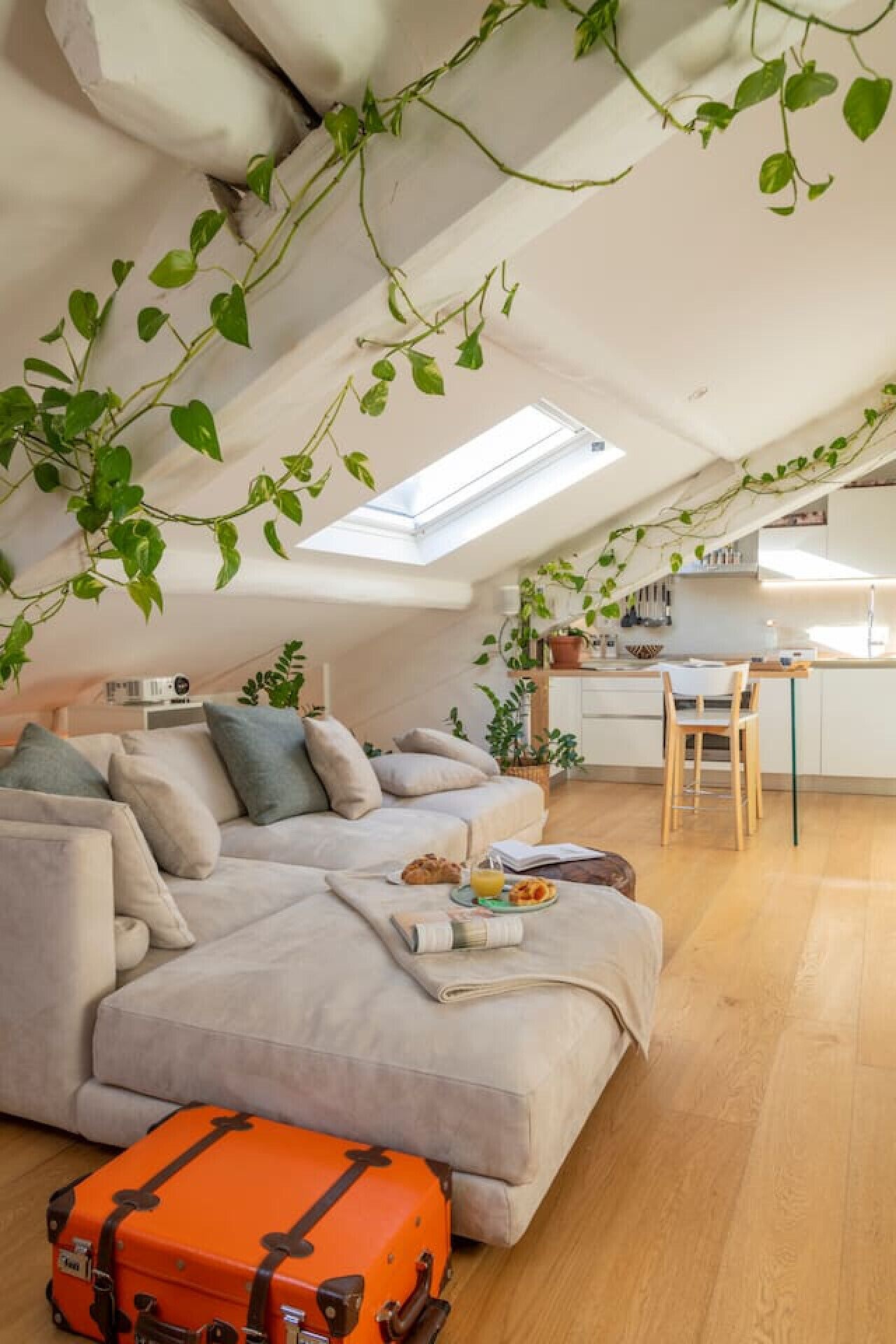 Un ambiente living in stile loft con soffitto alto, finestra a lucernario, divano, zona pranzo e cucina.