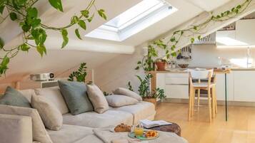 Un ambiente living in stile loft con soffitto alto, finestra a lucernario, divano, zona pranzo e cucina.