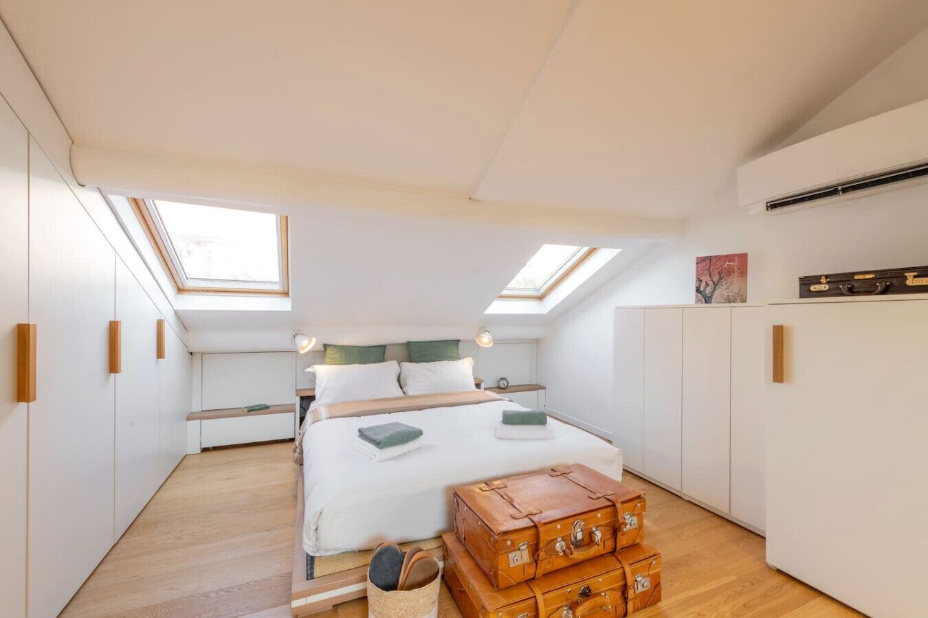 Une chambre avec un puits de lumière, un lit avec des oreillers, une table de chevet et une armoire.