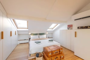 Un dormitorio con tragaluz, una cama con almohadas, una mesita de noche y un armario.
