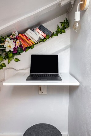 A laptop on a white shelf with a row of books and a light bulb on the wall.