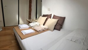 Ein ordentlich bezogenes Bett mit Kissen und gefalteten Handtüchern, ein Nachttisch aus Holz und eine Tür im Hintergrund.