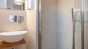 Ein modernes Badezimmer mit einer gläsernen Duschkabine, einem weißen Waschbecken und einem Spiegel.