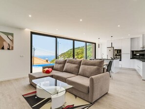 Ein modernes Wohnzimmer mit einer Couch, einem Glastisch und Blick auf eine Küstenlandschaft.