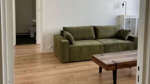 Et værelse med en grøn sofa, et træbord og en hvid væg.