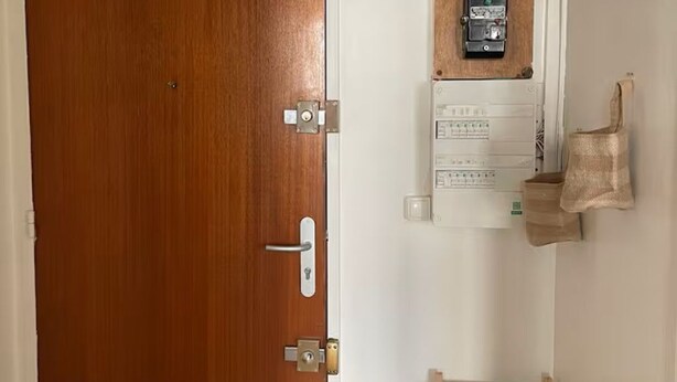 En trädør, et el-panel monteret på væggen, og en træhylde med en grøn kasse.