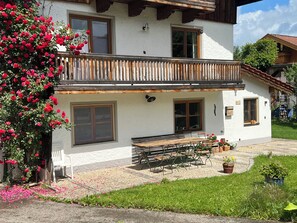 A two-story building with a balcony, large windows, and a garden area with a bench and potted plants. - Seehuber Vacation Rental (Siegsdorf)