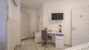 A bedroom with a bed, a desk, a chair, a television, and a door with a number.
