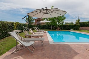 A swimming pool with lounge chairs and umbrellas, surrounded by greenery and a building in the background. - Apartment 'PoggioNovello-nord' with Private Pool, Wi-Fi and Air Conditioning (Peccioli)
