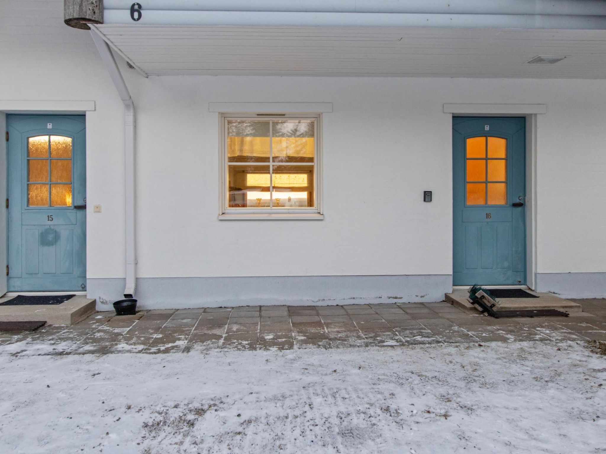 A white building with two blue doors, numbered 15 and 16, and a window between them.
