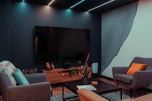 Ein modernes Wohnzimmer mit Flachbildfernseher, zwei Sesseln, einem Couchtisch und einer Holzkabine.