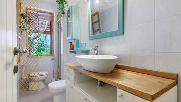 A bathroom with a white toilet, a white sink with a wooden countertop, and a mirror with lights.