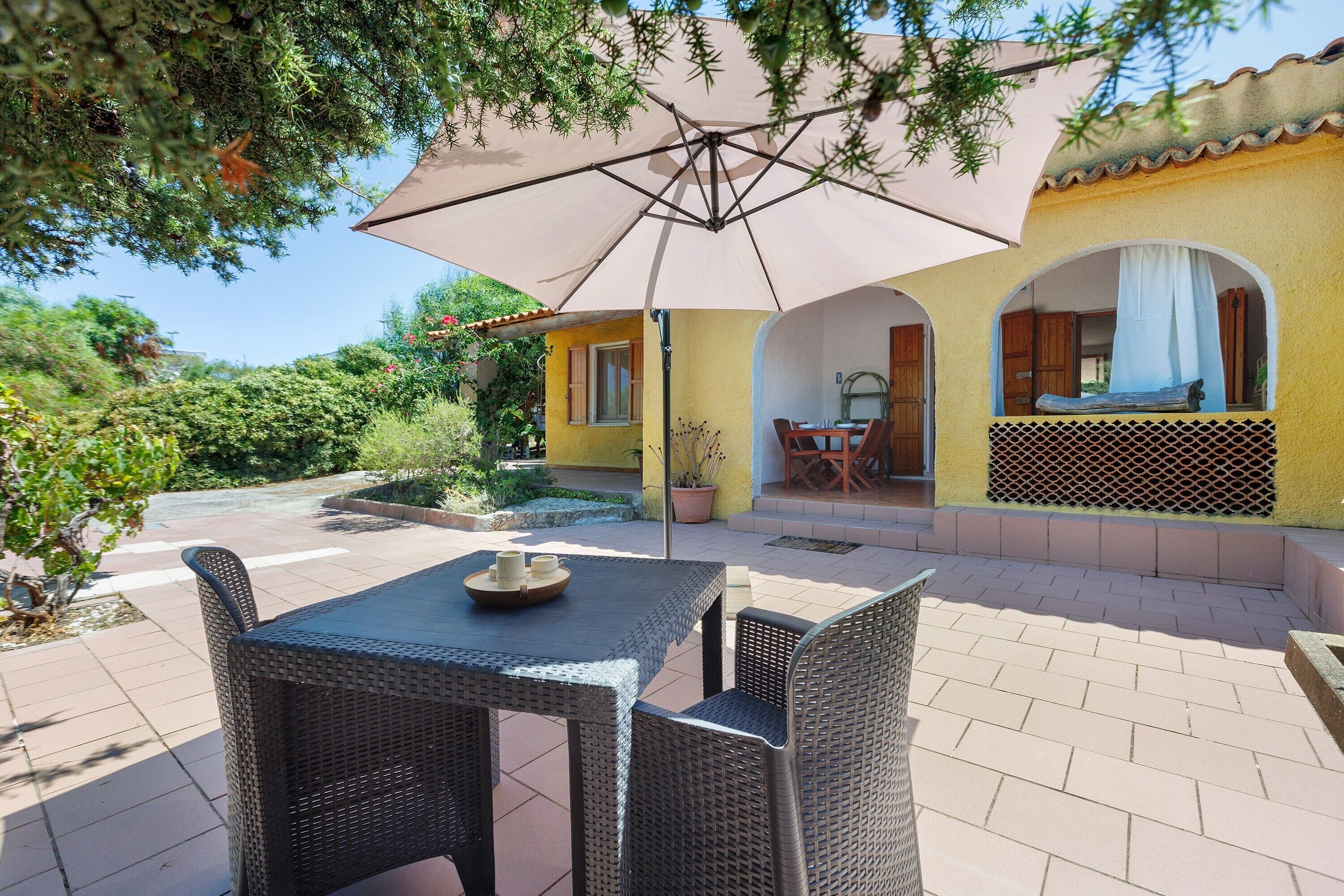 An outdoor patio with wicker furniture, a table with a bowl, and a large umbrella.