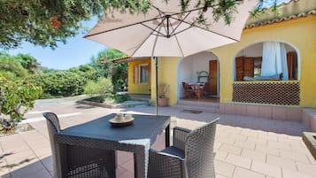 An outdoor patio with wicker furniture, a table with a bowl, and a large umbrella.