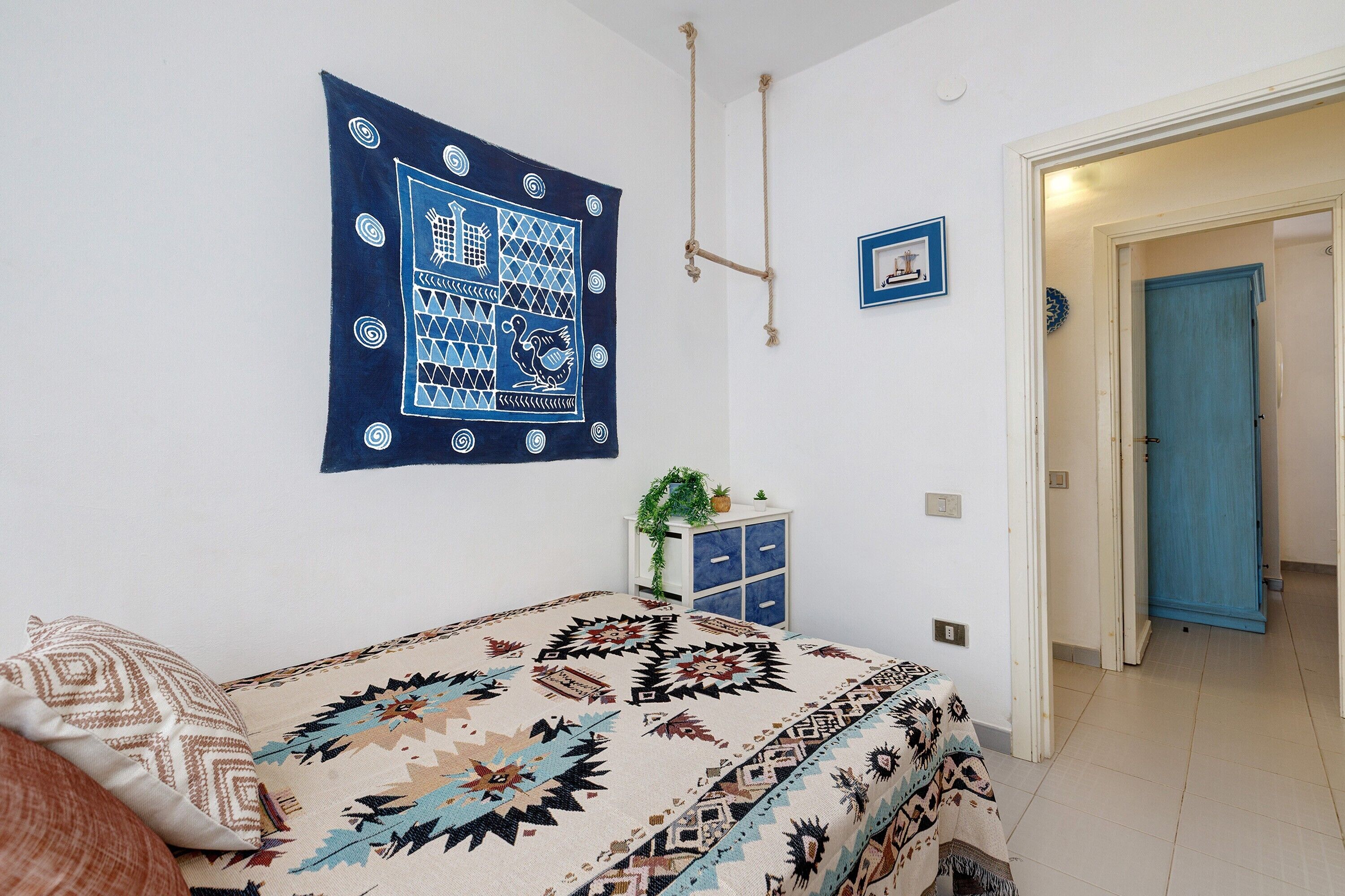 A bedroom with a bed, a wall tapestry, a small cabinet, and a door.