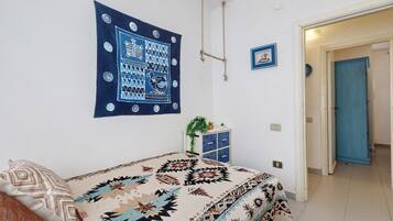 A bedroom with a bed, a wall tapestry, a small cabinet, and a door.