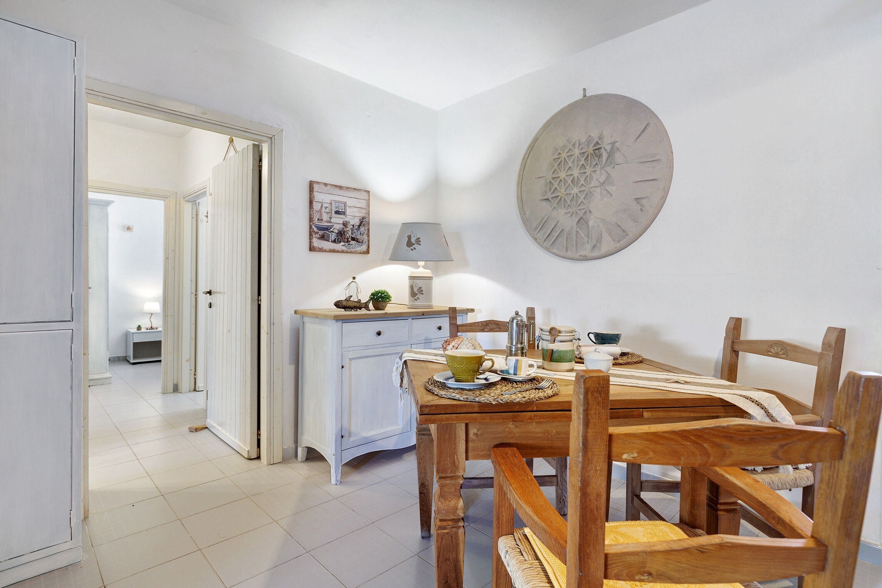 Uma sala de jantar com uma mesa de madeira, cadeiras, um abajur e um prato decorativo fixado na parede.