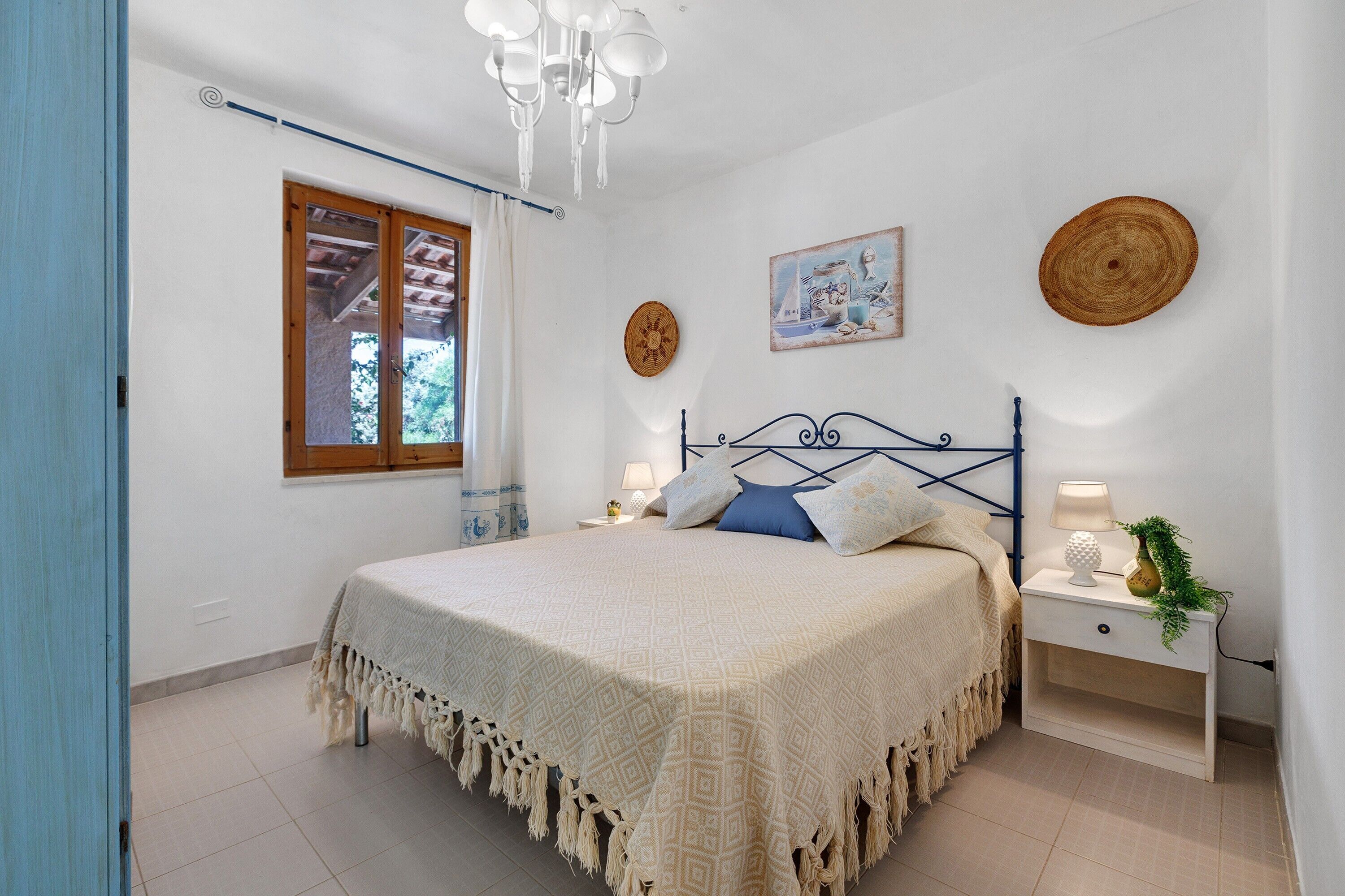 A bedroom with a bed, bedside tables, a window, and a chandelier.
