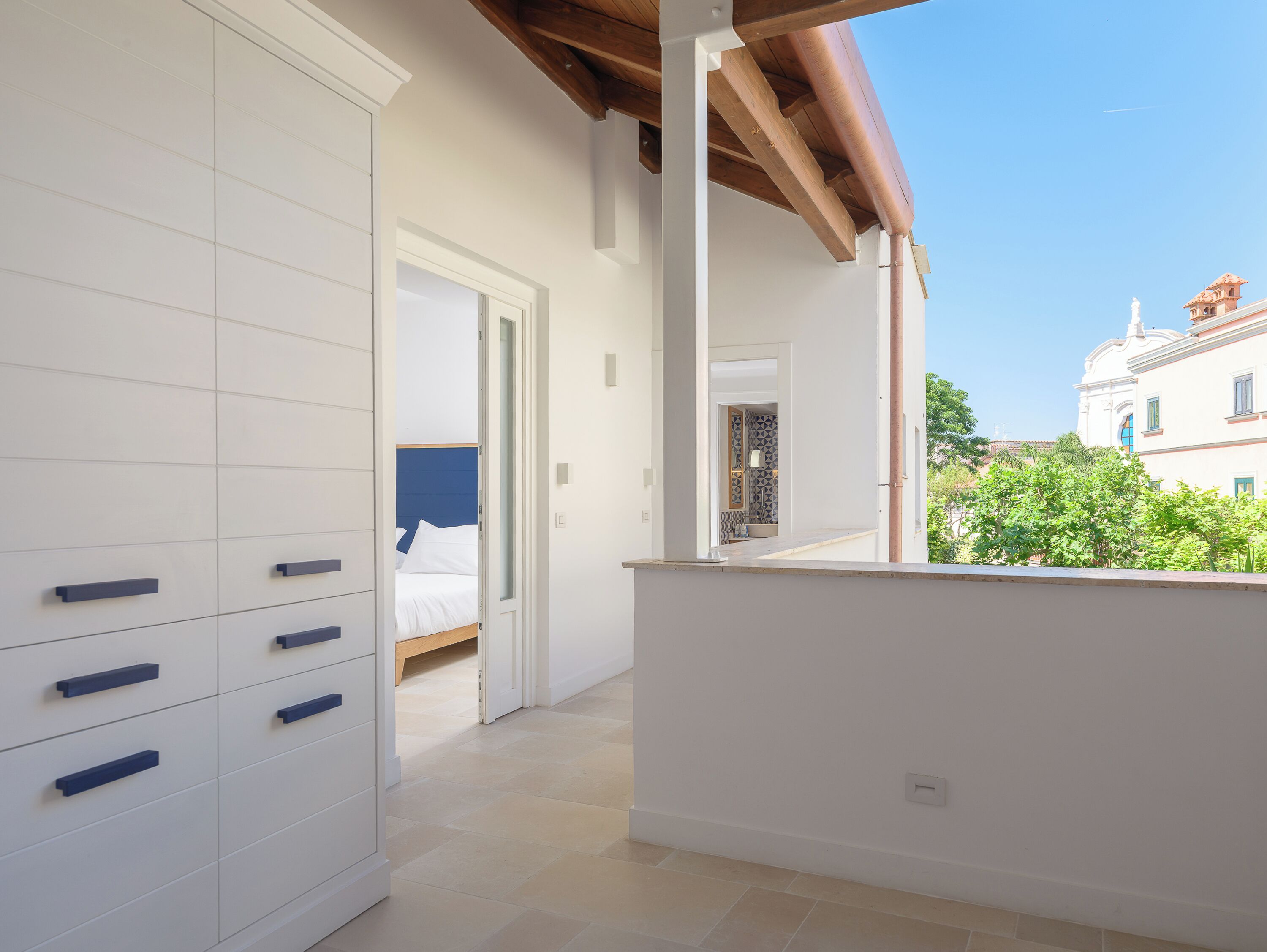 Una habitación con una cama, un armario blanco y vista a un edificio al fondo.