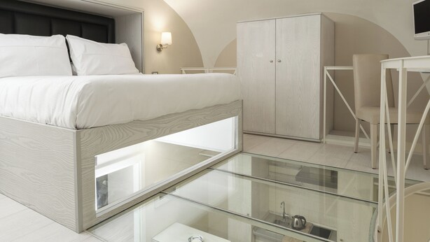 Une chambre moderne comprenant un lit, une armoire, un bureau et une salle de bain fermée par des parois de verre.