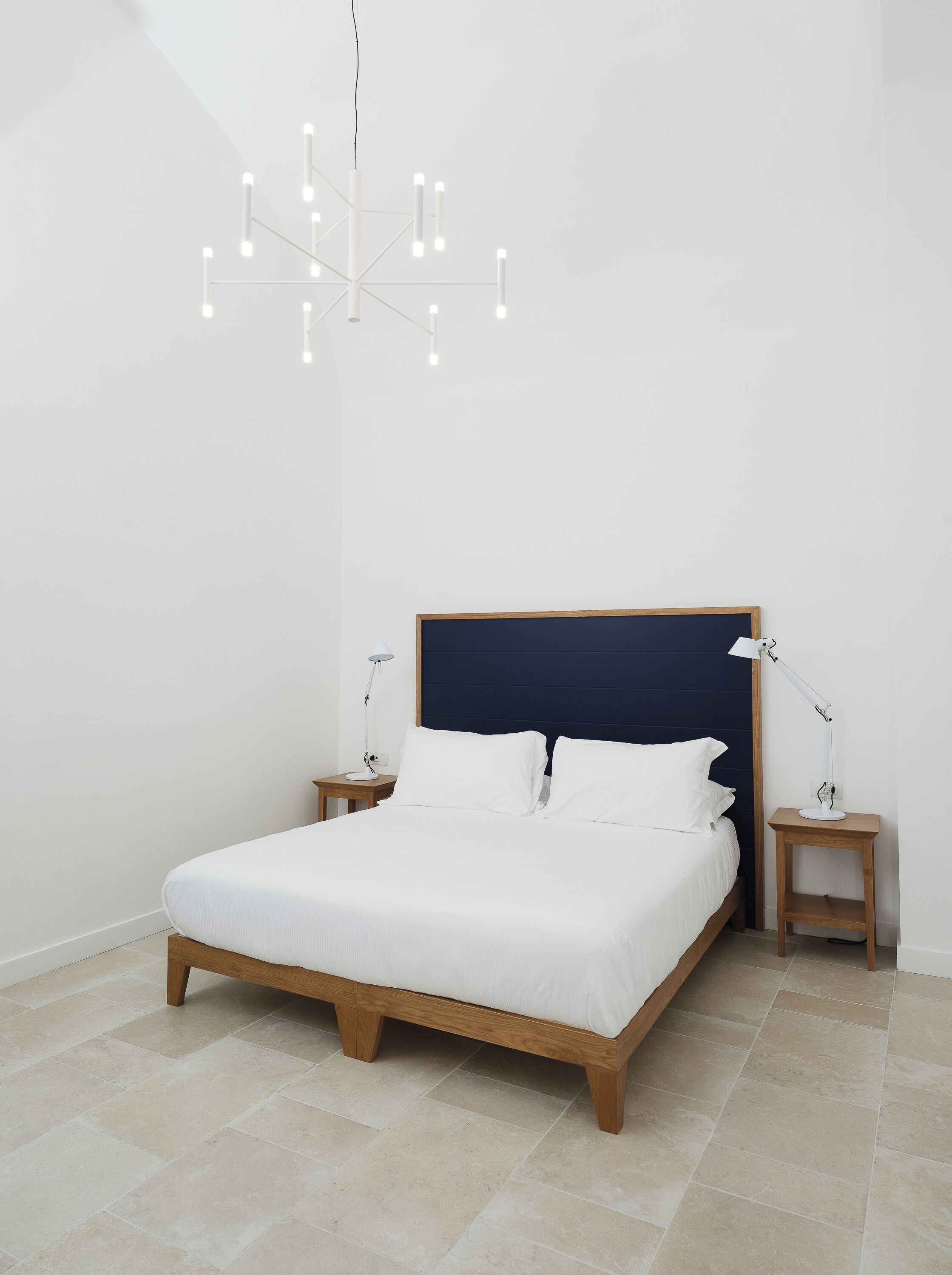 A bedroom with a bed, bedside tables, a modern chandelier, and a dark headboard.