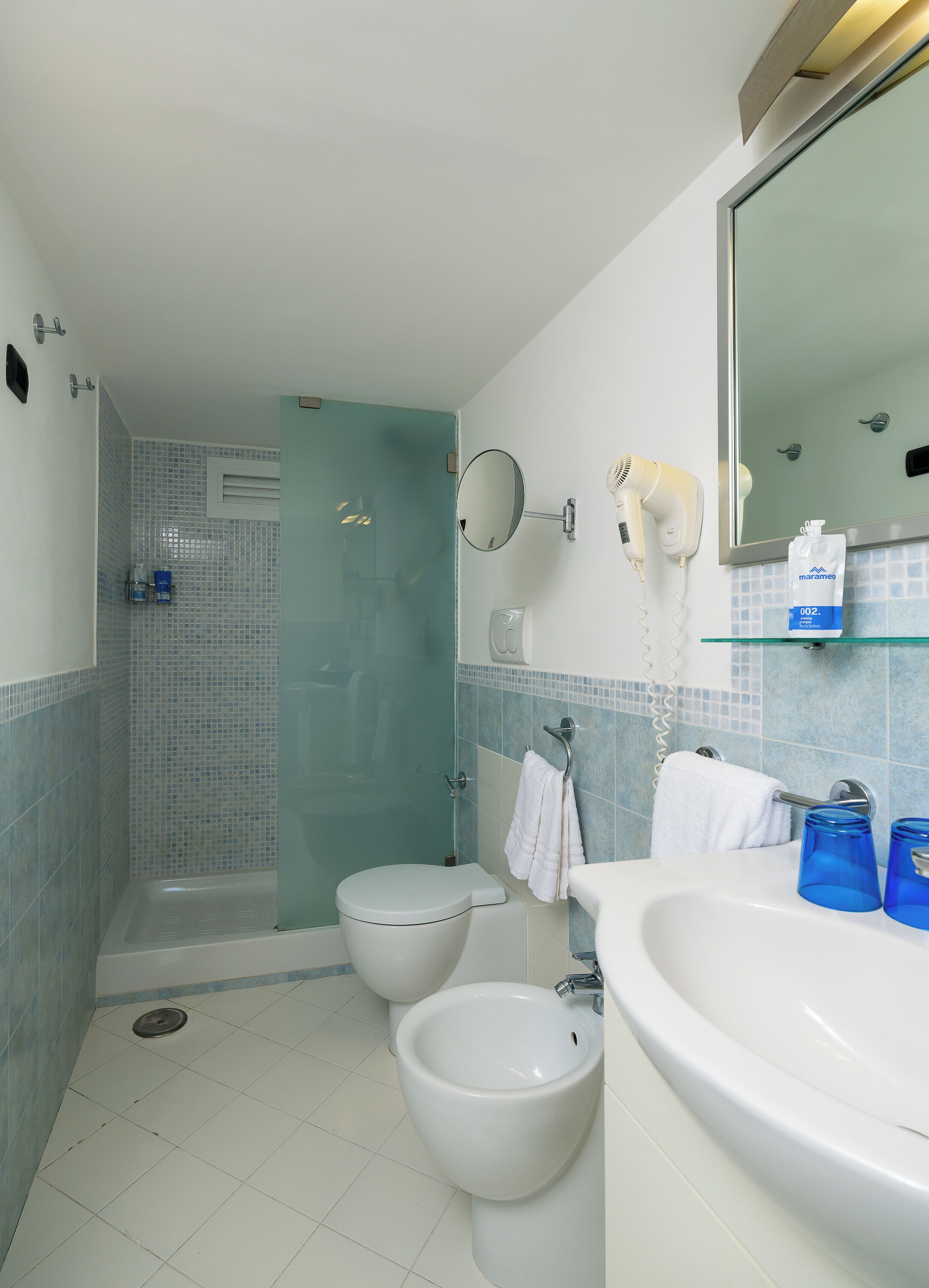 Ein Badezimmer mit Dusche, zwei Toiletten, einem Bidet, einem Waschbecken, einem Spiegel und einem Fön.