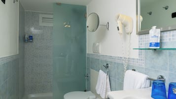 A bathroom with a shower, two toilets, a bidet, a sink, a mirror, and a hairdryer.
