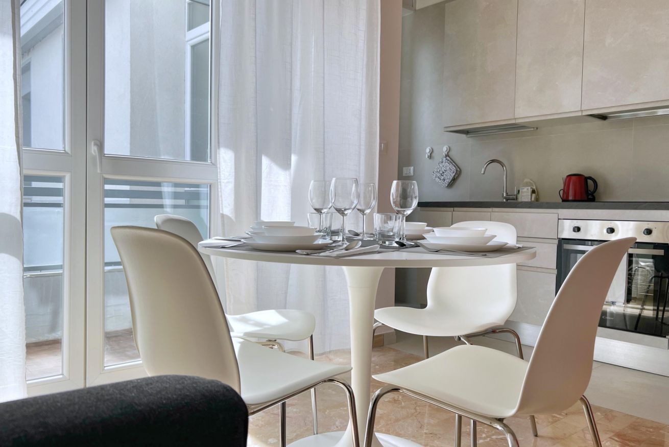 Una cocina moderna con comedor, que incluye una mesa preparada para cuatro personas, sillas y vistas al exterior.