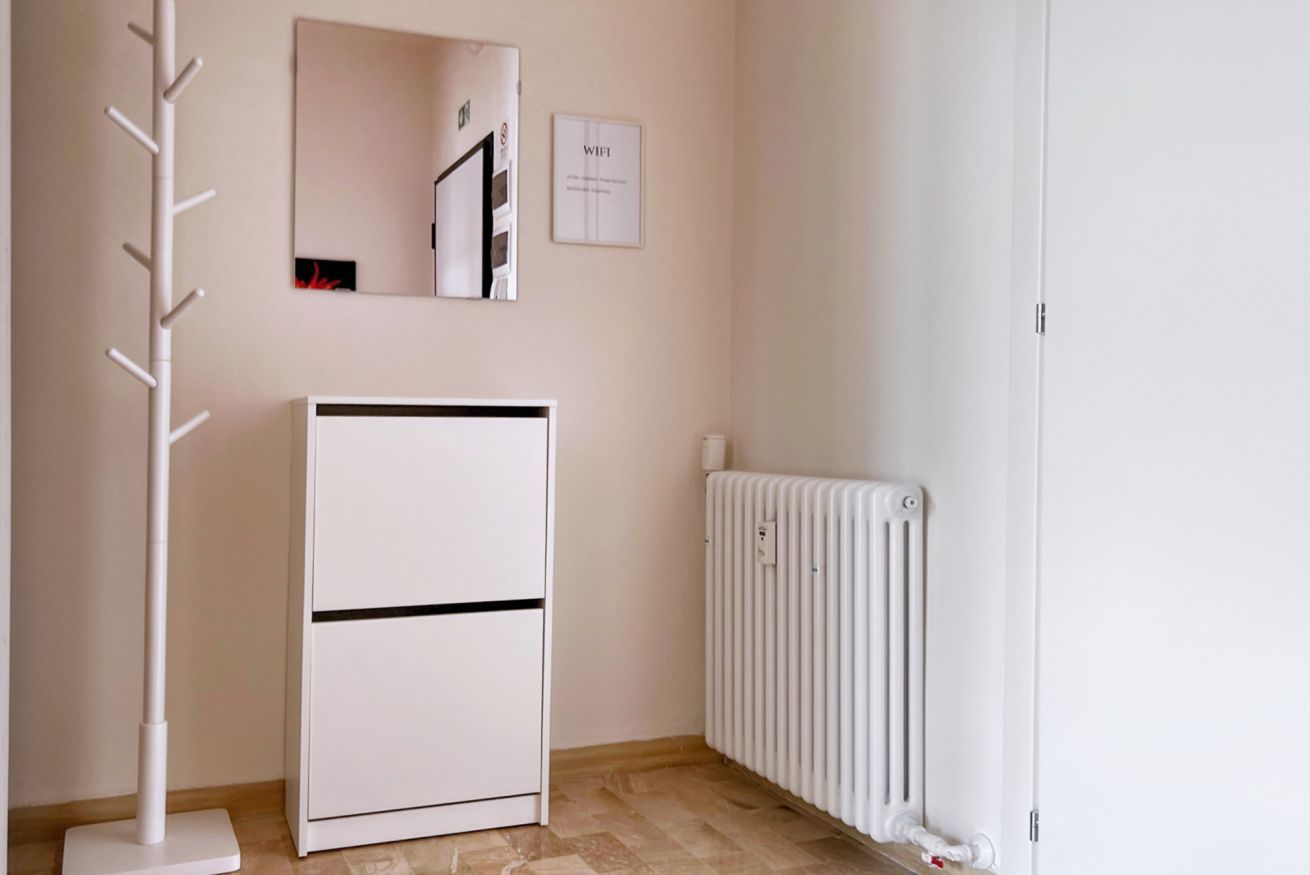 A room with a white radiator, a white stand-alone heater, and a coat rack.