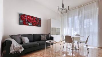 A modern living room with a sofa, a small round table, and a dining area with chairs.