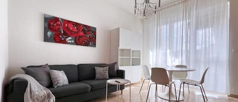 A modern living room with a sofa, a small round table, and a dining area with chairs.