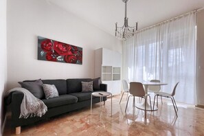 Ein modernes Wohnzimmer mit einer Couch, einem kleinen runden Tisch und einem Essbereich mit Stühlen.