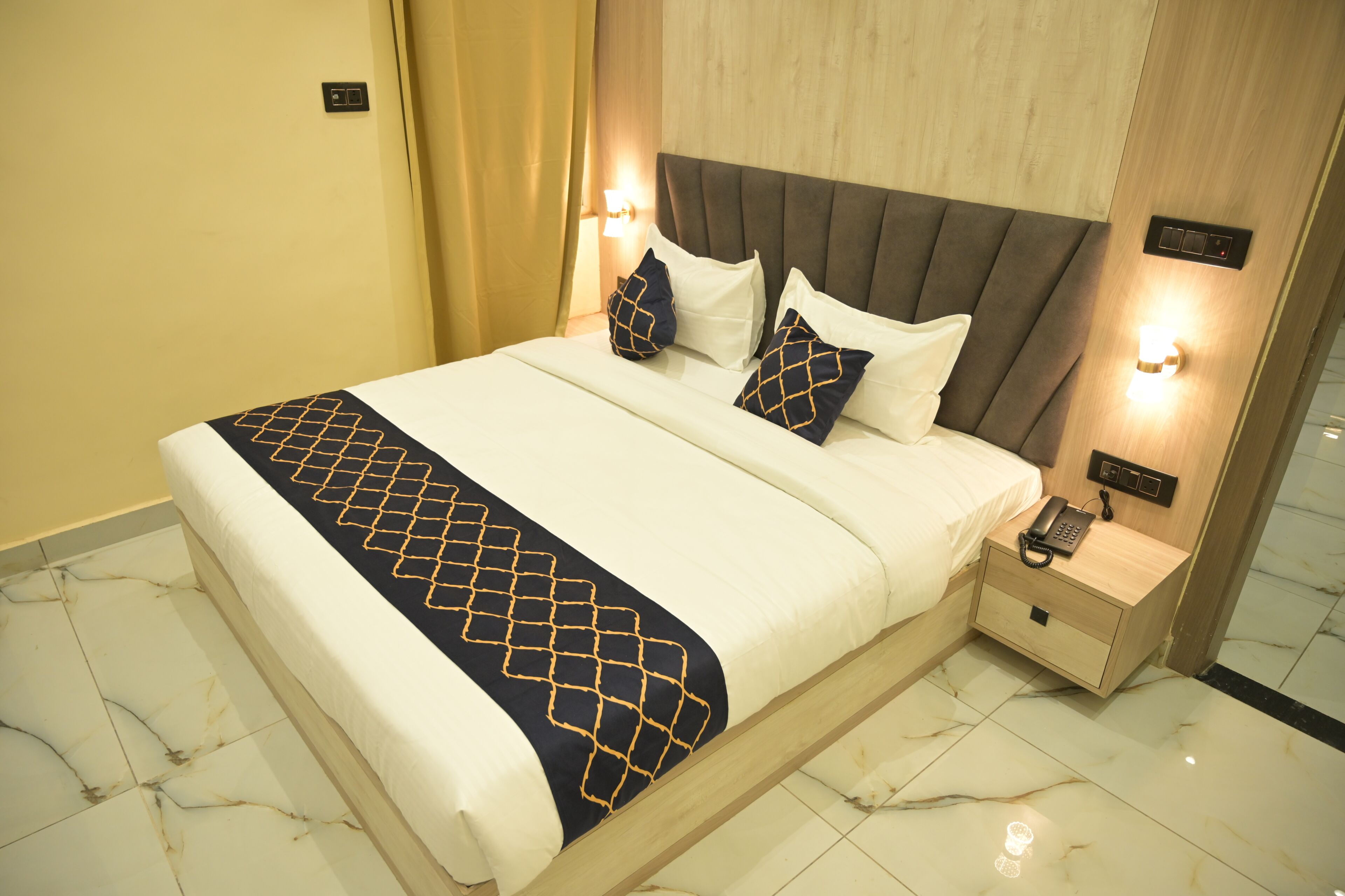 Een hotelkamer met een bed, nachtkastjes, een telefoon en een wandlamp.