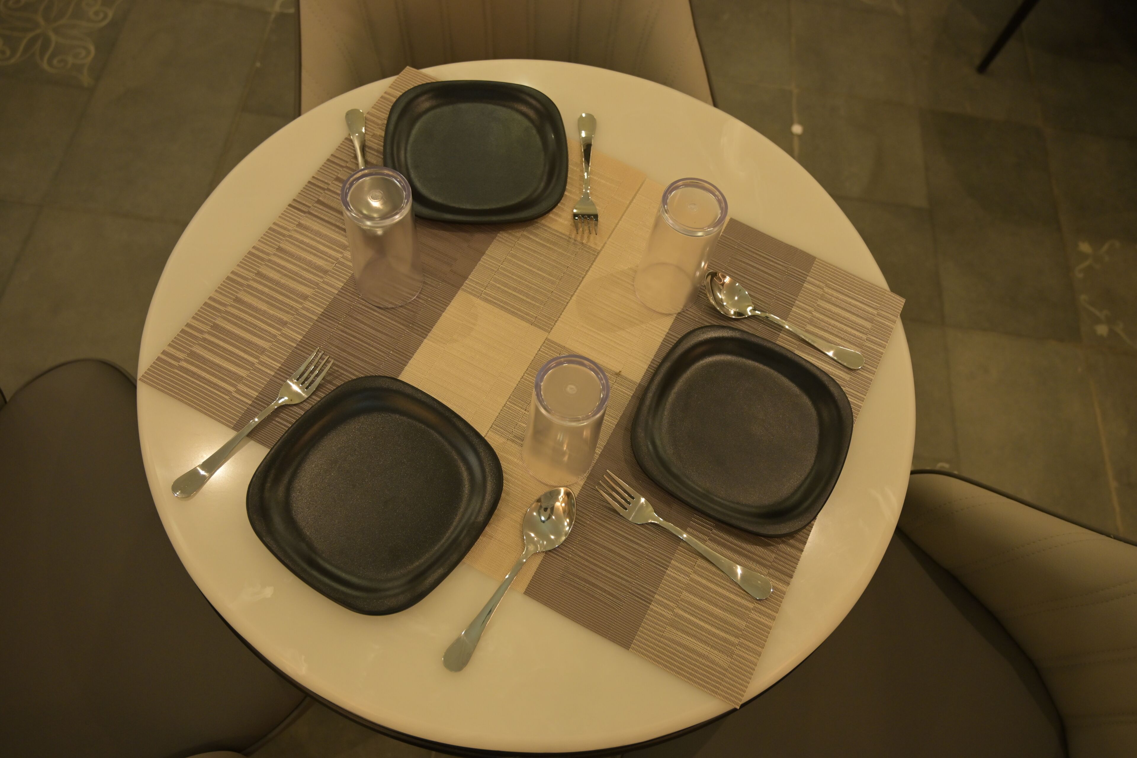 A round dining table with four plates, two forks, two spoons, and two glasses.