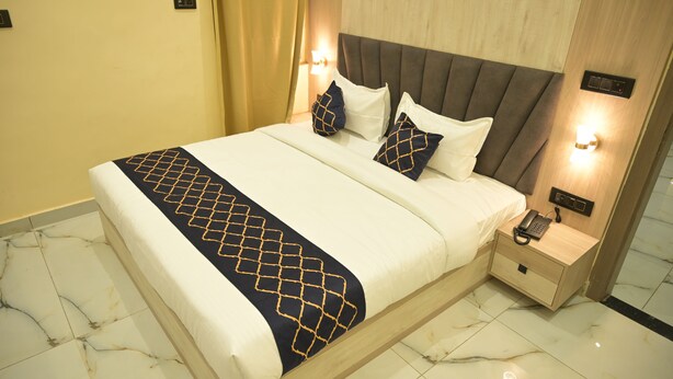 Una cama bien hecha con una colcha de estampado geométrico, un cabecero de madera, lámparas de noche y una mesita con un teléfono.