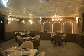 Un comedor con mesas y sillas redondas, una recepción con un letrero de neón y un techo con diseño de cuadrícula.