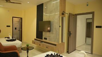 A hotel room with a bed, a seating area with a chair, a small table, a television mounted on a marble wall, and a door leading to another room.