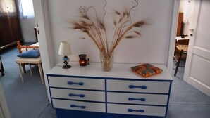 A white and blue dresser with a vase of dried plants, a lamp, and a small table with a cushion.