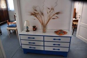A white and blue dresser with a vase of dried plants, a lamp, and a small table with a cushion.