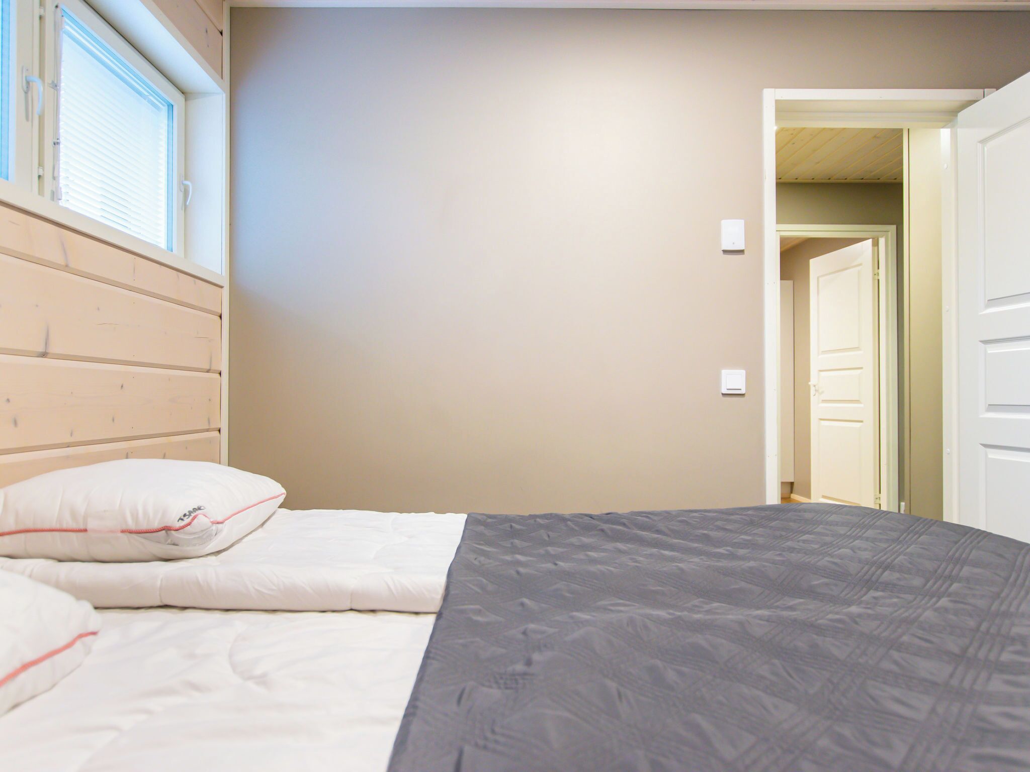 A bedroom with a wooden headboard, a bed with white and gray bedding, and a door leading to another room.
