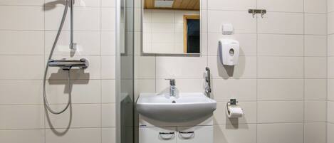 A bathroom with a shower, sink, mirror, toilet, and trash bin.