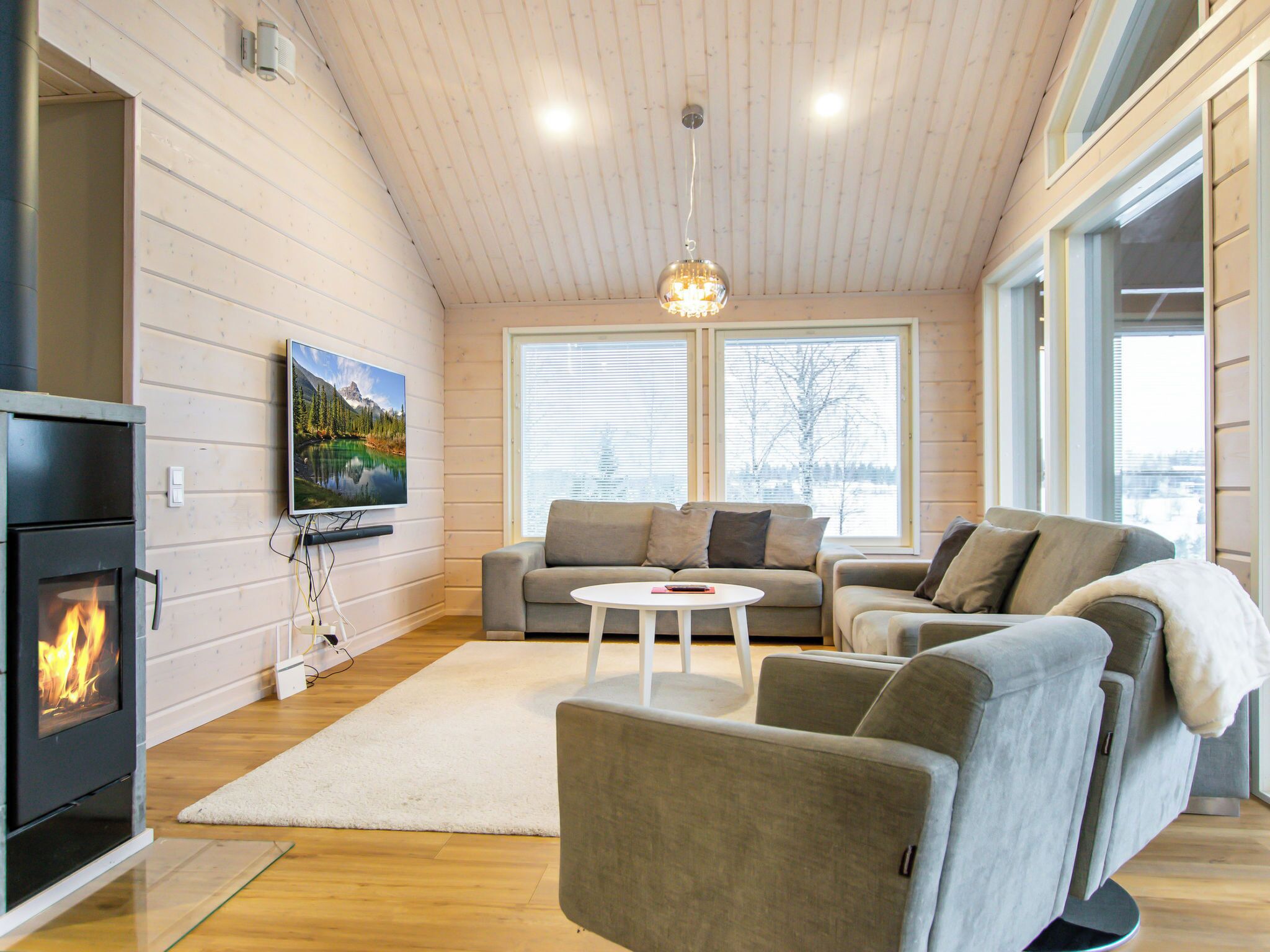 A cozy living room with a fireplace, a sofa, a coffee table, and large windows.