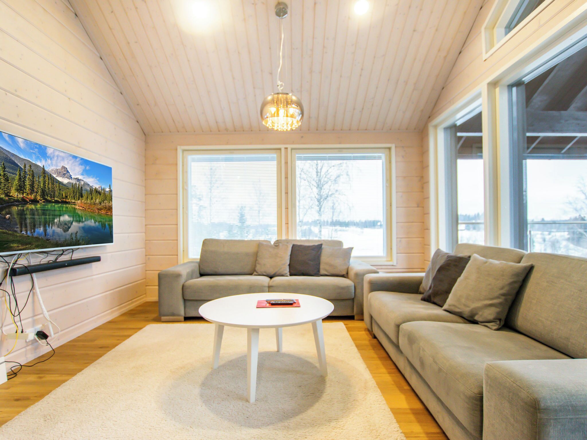En moderne stue med et stort fladskærms-tv, to sofaer, et sofabord og store vinduer.