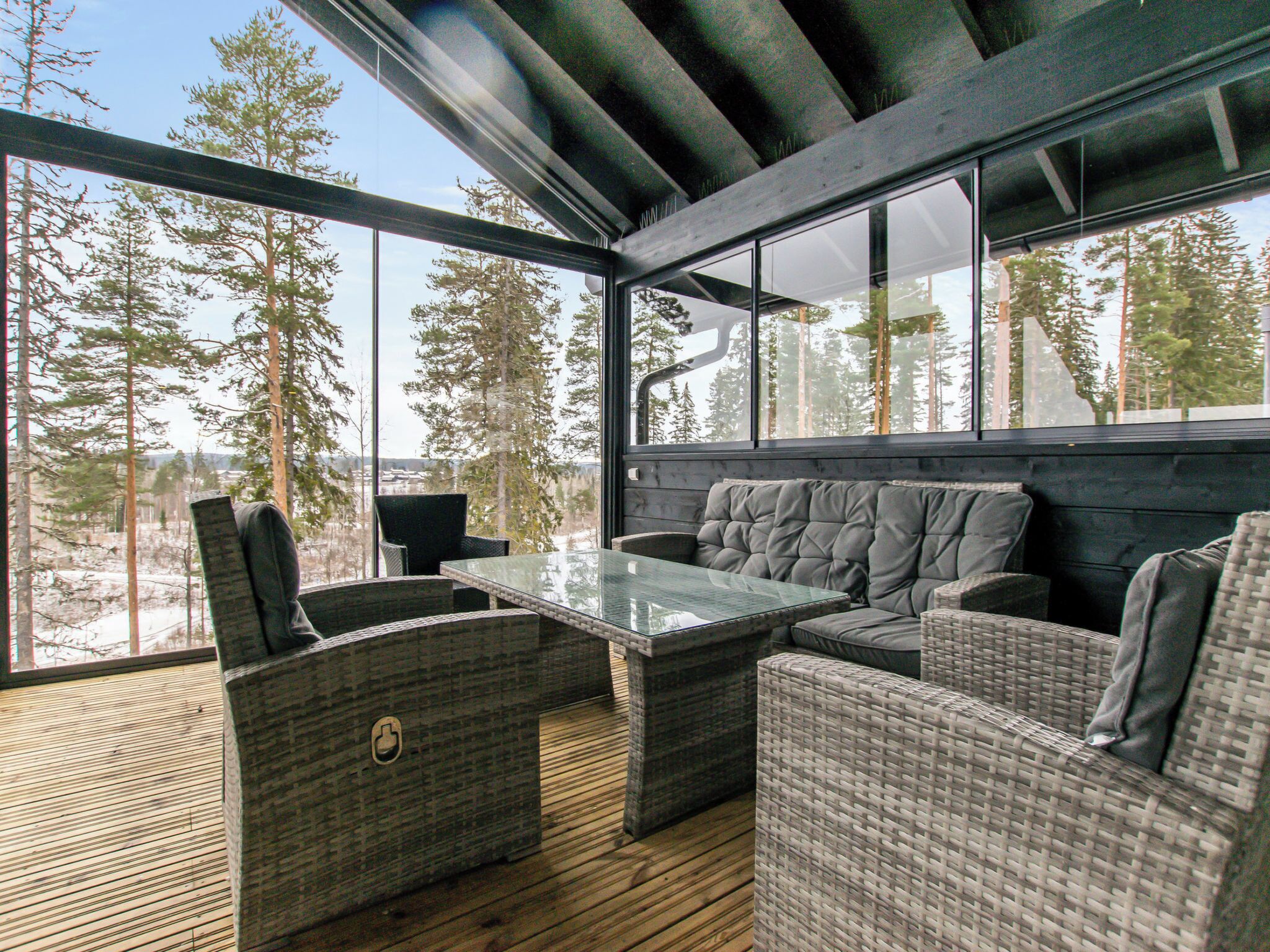 Un espacio moderno al aire libre con mobiliario de mimbre y una mesa de vidrio, con vista a un paisaje boscoso.