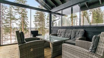Un espacio moderno al aire libre con mobiliario de mimbre y una mesa de vidrio, con vista a un paisaje boscoso.