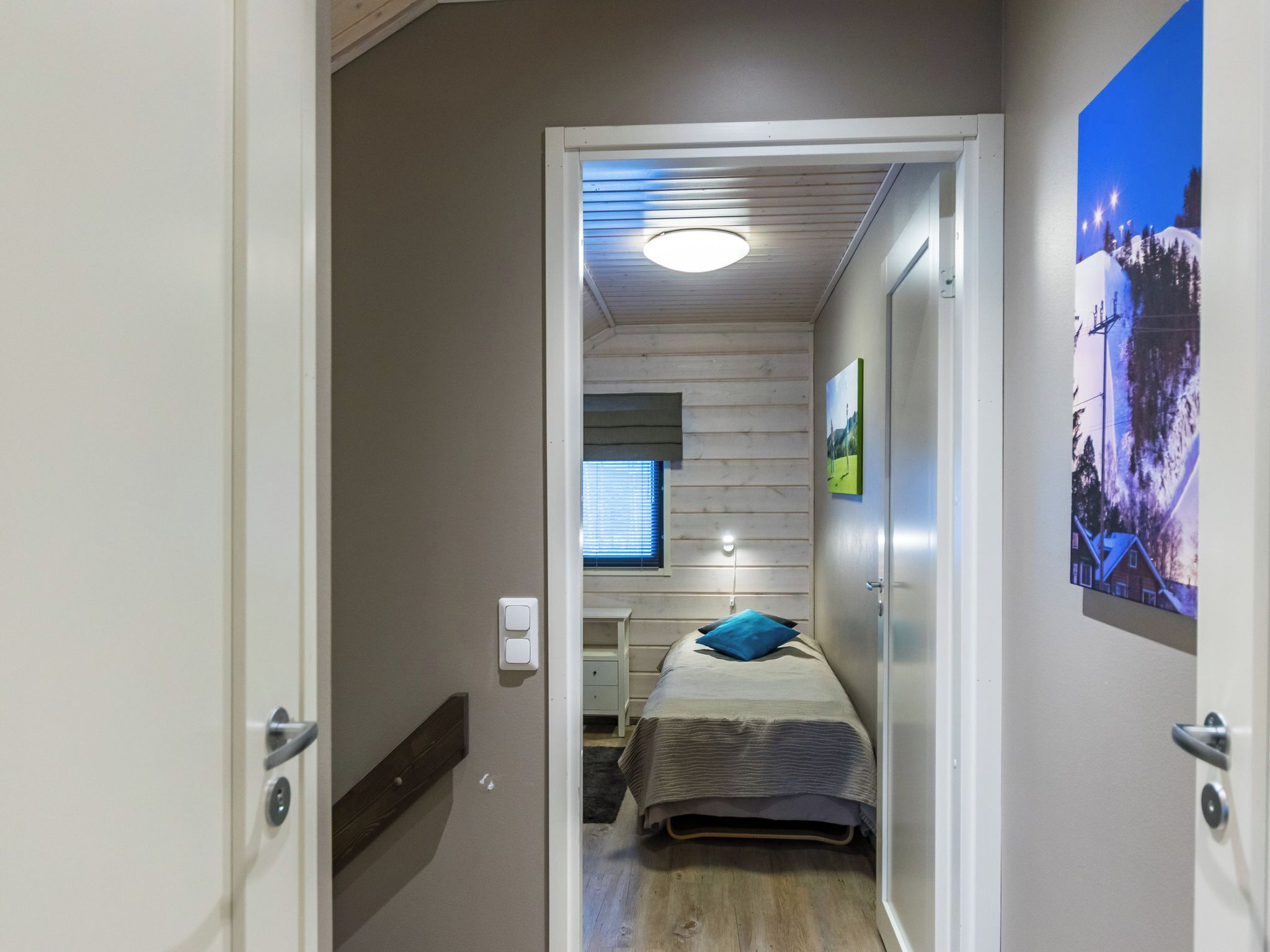 A narrow hallway leading to a bedroom with a bed, a window, and a wall-mounted light fixture.