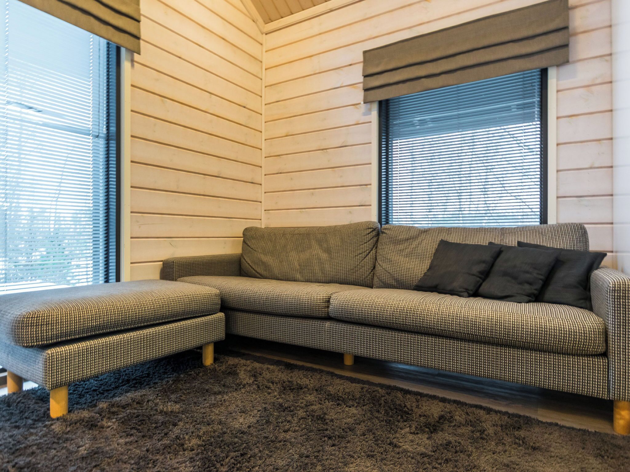 A sectional sofa with a checkered pattern, a dark rug, and wooden legs.