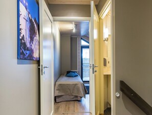 A narrow hallway leading to a bedroom with a bed, a door, and a wall-mounted picture.