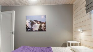 Ein Schlafzimmer mit einem Bett, einem kleinen Nachttisch, einer Wandleuchte und einem Gemälde einer verschneiten Landschaft.