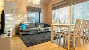 A modern interior with a wooden ceiling, a sofa, a dining table with chairs, and large windows.